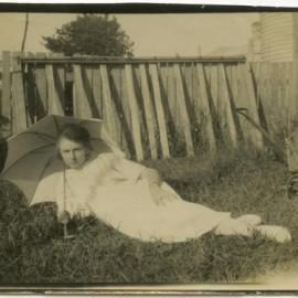 Photograph of unidentified girl in white reclining in yard with umbrella