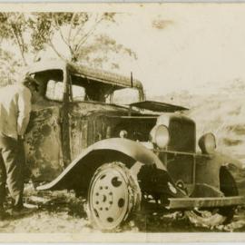 Two men inspecting burnt out car.