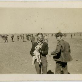 A man holding a young goat, somewhere in a desert