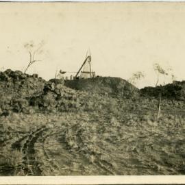 Picture of a muddy field with an uncertain construction behind a berm of earth. Location unknown.
