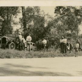 Photo of cars by the road, with people milling about, location unknown.