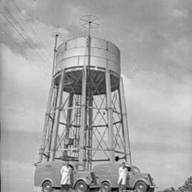 Two men standing next to Kloster's vans near a tower, NSW, 1958