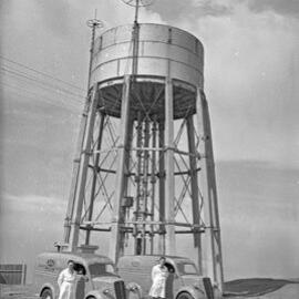 Two men standing next to Kloster's Proprietary Limited vans near tank, NSW, 1958 