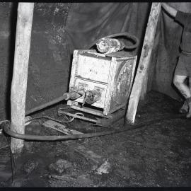 Miner standing next to electrical box and cables, Burwood [No 3] Colliery, Whitebridge, NSW,  1957