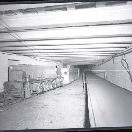 Coalcliff Colliery, man driving an engine alongside a conveyor belt underground, NSW, 1959