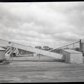 Outside factory buildings with conveyor belts, 1963
