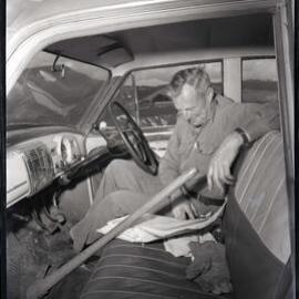 A man in his car reading paperwork, 1963