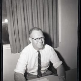 Man at desk in tie smiling, 1963