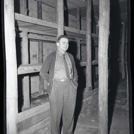 Man standing in area with wooden shelves, [Bellambi, NSW] 1963