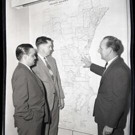 Three men standing in front of colliery holdings map, 1963