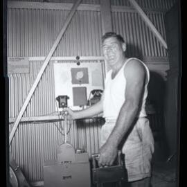 Worker operating equipment with two telephones in the background, 1963