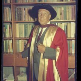 Gentleman in academic dress in front of book case 
