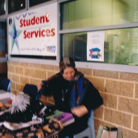 An unidentified staff member manning the psychic-themed Student Services table at a Central Coast Campus open day [n.d.] [Same person as previous image 01566]
