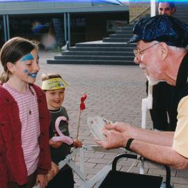 Unidentified children watching an unidentified person performing a card trick at a Central Coast Campus open day. Image taken before the information common was built onto the front of the library [Same people as previous image 01554] [n.d.]
