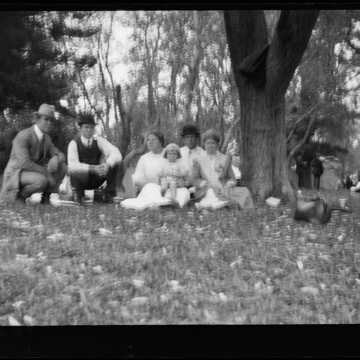 Family group sitting under tree, c1910s.