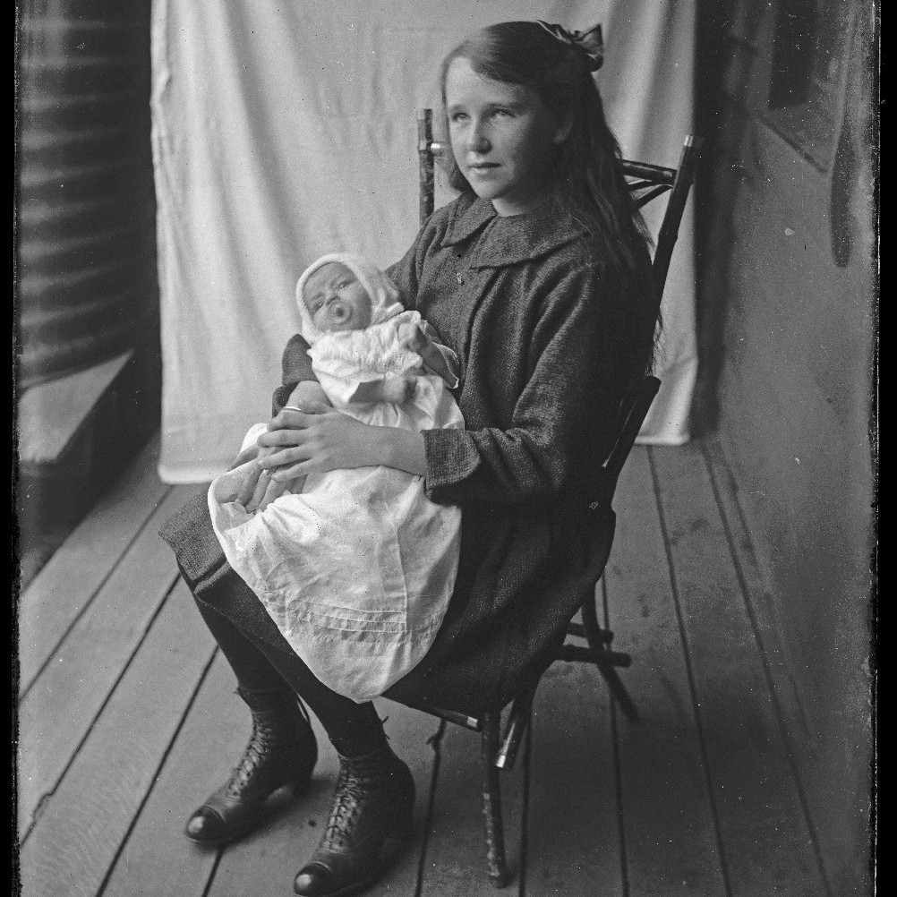 Young girl with infant, on ornate cane chair, c1910s