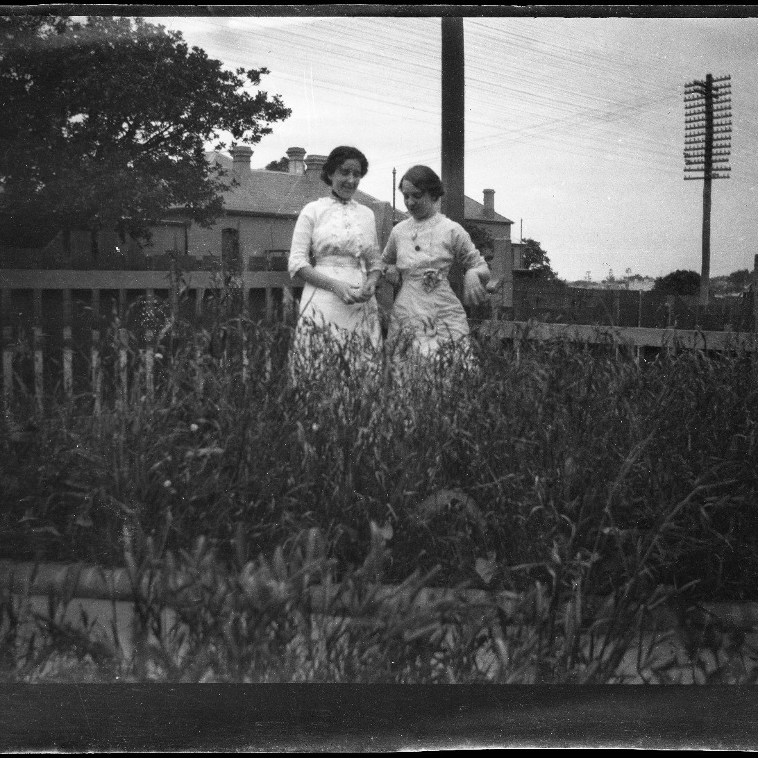 Two women standing near fence in overgrown grass