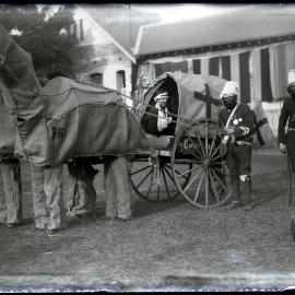 Red Cross Ambulance (comical) drawn by men dressed as horses, and attended by bearded guards, c.1914