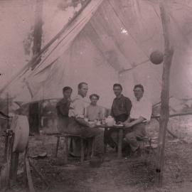 Men at camp site with axe grinder in foreground