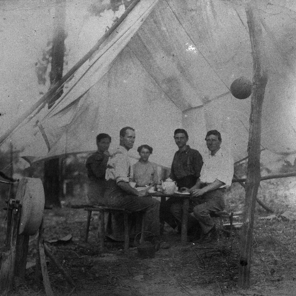 Men at camp site with axe grinder in foreground