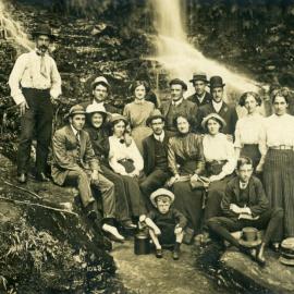 Group of people in front of a waterfall. Postcard, c. 1908