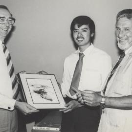 Vice-Chancellor, Professor Keith Morgan is presented with a picture by an unidentified man and University Librarian, Ted Flowers (right), the University of Newcastle, Australia