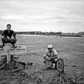 Two gentlemen inspecting damage from the Maitland Flood, 1955. One is sitting on the sign marking the boundary between the City of Maitland and the Shire of Lower Hunter: Lucey Collection