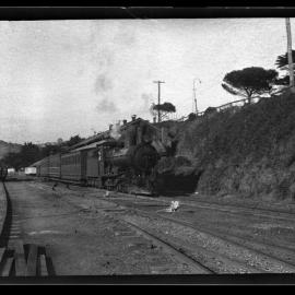 TGR Ab Class, hauling passenger train past tin shed on embankment, small town in background, unidentified location [n.d.]