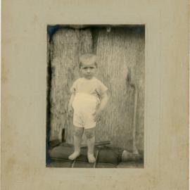 A toddler standing upright dressed in light coloured clothing, [n.d.]